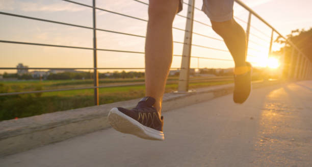 istock LOW ANGLE: Unrecognizable young man jogs across asphalt bridge at golden sunset. 1300970714