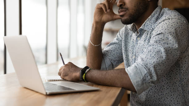 istock Pensive young black man sit at desk before pc screen 1300971898