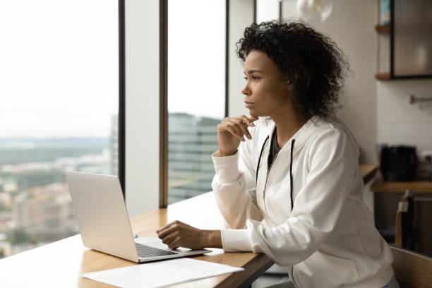 istock Millennial black woman sit by laptop think look at window 1300972456
