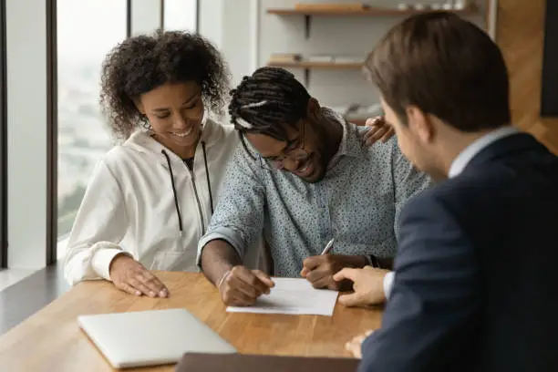 Happy african couple consulting with trusted expert lawyer sign life insurance contract. Professional salesman agent close deal with black family clients show place to put signature on paper agreement