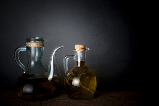 Extra virgin olive oil. Two oil pitcher with extra virgin olive oil flavored with rower and garlic on a dark background.