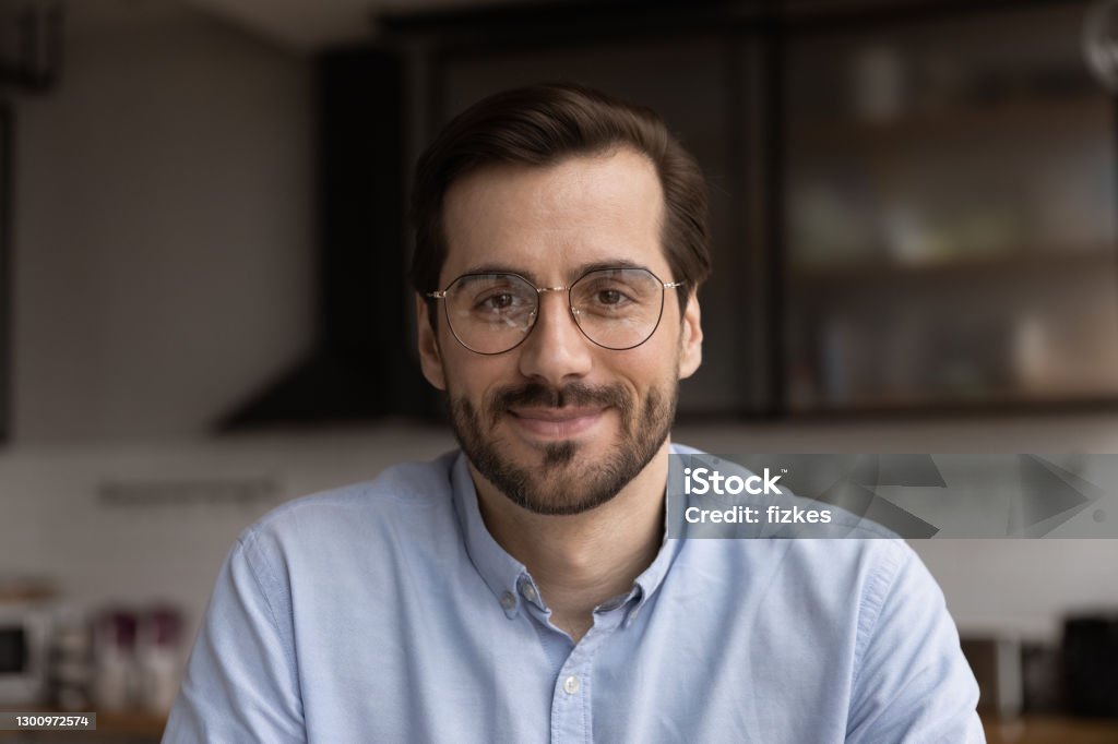 Millennial male team leader organize virtual workshop with employees online Portrait of young smiling handsome bearded man in glasses looking at camera chatting with wife friend by videocall. Millennial male team leader organize virtual meeting workshop with employees online Profile View Stock Photo