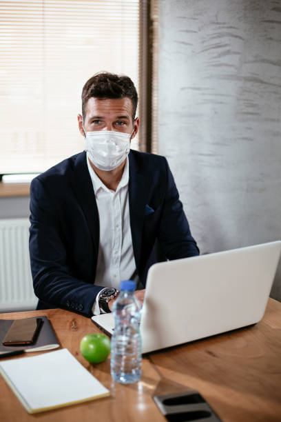 istock Young businessman with a mask working in his office on laptop. 1300972815