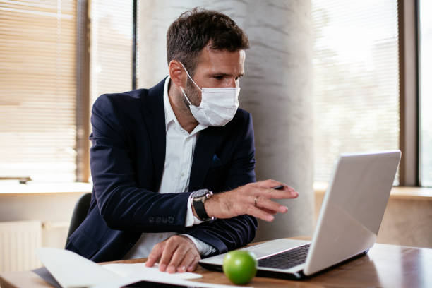 istock Young businessman with a mask working in his office on laptop. 1300972942