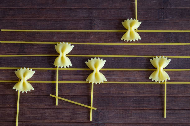 Creative composition of a sheet of a musical score, the notes are created with raw butterfly-shaped paste resting on a wooden background and the stripes with spaghetti.