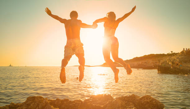 istock LENS FLARE: Golden sun rays shine on couple holding hands while diving into sea. 1300974604