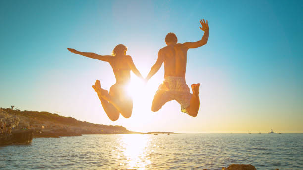 istock LENS FLARE: Carefree tourists hold hands while jumping into the refreshing sea 1300974635