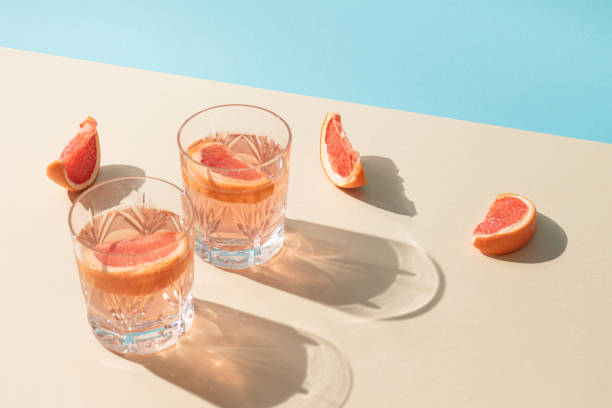 明るいベージュと青い背景に新鮮なグレープフルーツのスライスとドリンクの2杯。創造的な最小限の夏のコンセプト。晴れた日の影。 - ガラス 写真 ストックフォトと画像