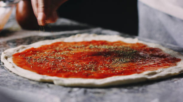 istock hand puts oregano on pizza with tomato 1300975115