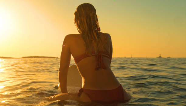istock CLOSE UP: Unrecognizable surfer girl sits on surfboard and observes the sunset 1300975185