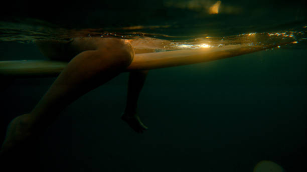 istock UNDERWATER: Golden sunset shines on unrecognizable woman sitting on surfboard 1300975218