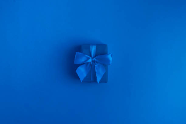 istock Blue gift box with blue ribbon over classic blue background. Trendy color 1300975298