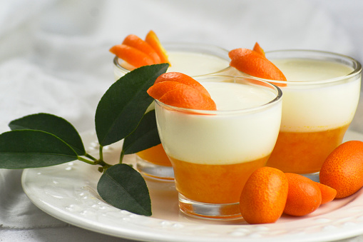 Tasty panna cotta dessert with mandarin jelly decorated with fresh slices of fruits on white background.