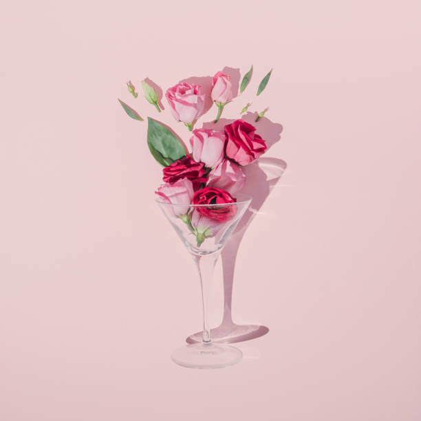 composição romântica do dia dos namorados feita com copo de coquetel, folhas verdes e rosas rosas no fundo pastel. mínima de leito plano. - flower drink - fotografias e filmes do acervo