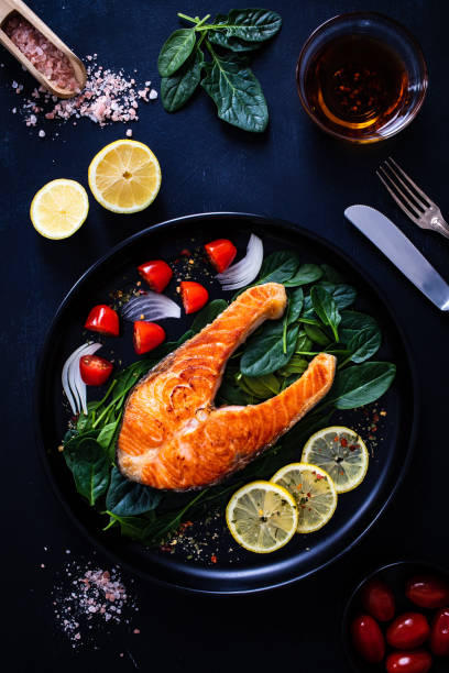 istock Fried salmon steak and fresh vegetables on wooden black table 1300984509