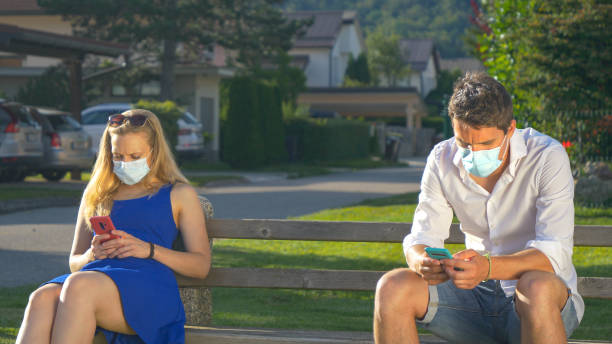 istock CLOSE UP: Two strangers wear facemasks while sitting on park bench and texting. 1300985757