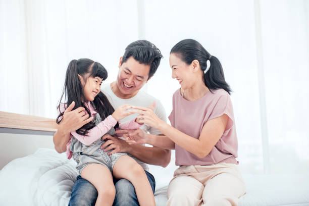 Happy Asian family playing together on bed while smile in bedroom at home. Happy Asian family (mother, father, child daughter) playing together on bed while smile in bedroom at home. asian ethnicity family stock pictures, royalty-free photos & images
