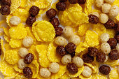 Yellow cornflakes and chocolate balls with milk as background for design