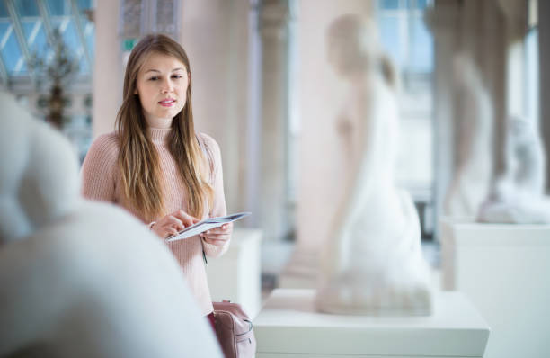 istock Girl looking with interest at ancient sculptures in museum, using guidebook 1300987334