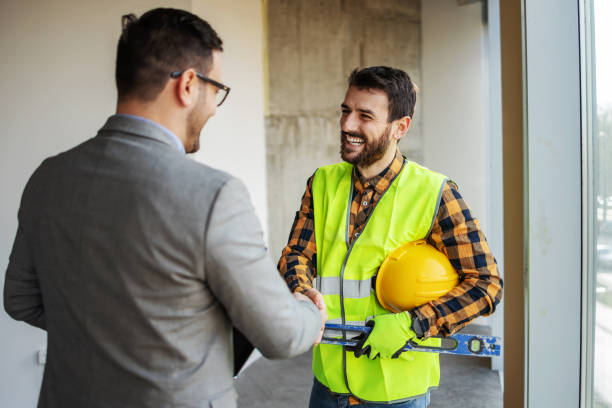 улыбающийся строитель пожимает руку начальнику, стоя в здании в процессе строительства. - building contractor стоковые фото и изображения