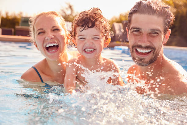 portrait of family with young son having fun on summer vacation splashing in outdoor swimming pool - floating on water fotos imagens e fotografias de stock