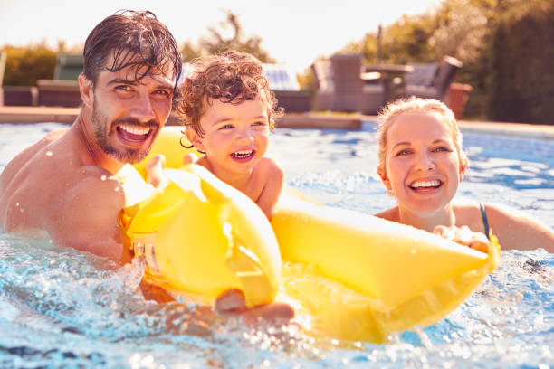 屋外スイミングプールで夏休みにインフレータブルで楽しんでいる若い息子との家族 - floating on water women swimming pool water ストックフォトと画像