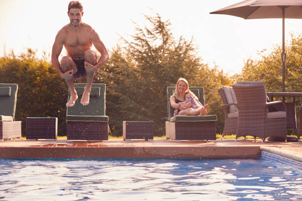 le père saute dans la piscine extérieure sur des vacances d’été regardées par la mère et le fils - cannon photos et images de collection