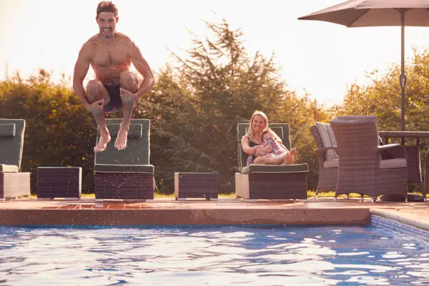 Photo of Father Jumps Into Outdoor Pool On Summer Vacation Watched By Mother And Son
