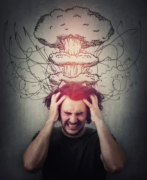 Photo of Head explosion metaphor. Bewildered man messing up and pulling his hair,  eyes closed screaming and clenching teeth. Suffering headache, dementia disease. Mental health concept, migraine and anxiety