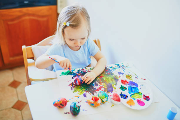 Adorable little girl painting eggs for Easter at home, in kindergaten or preschool. Celebrating holidays with children. Creative activities and games for kids. Stay at home entertainment