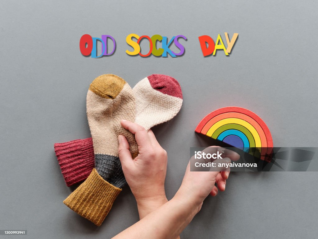 Odd Socks Day. Hand hold pair of mismatched socks. Wooden rainbow, toy figures. Social initiative against bullying in school or workplace. Design for anti-bullying campaign promotion poster Odd Socks Day. Hand hold pair of mismatched socks. Wooden rainbow, toy figures. Social initiative against bullying in school or workplace. Promotion design for anti-bullying campaign. Bizarre Stock Photo