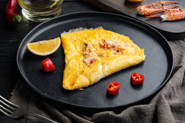 istock Thai  Asian omelette, fresh red chilli, brown and white crabmeat, lemon, Cheddar cheese, eggs, on plate, on black wooden table background 1300994134