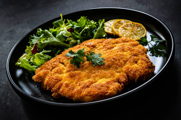 istock Fried pork chop with lemon and fresh vegetables on black table 1300995556