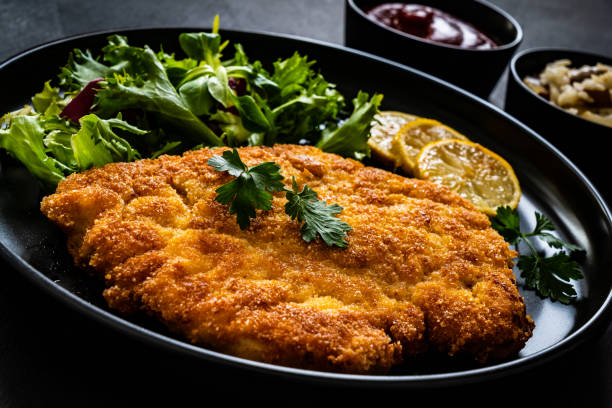 smażony kotlet schabowy z cytryną i świeżymi warzywami na czarnym stole - wiener schnitzel zdjęcia i obrazy z banku zdjęć