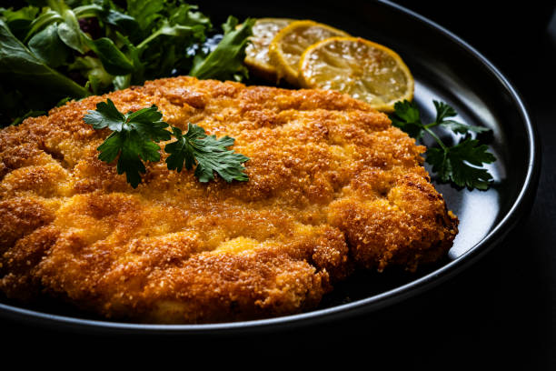 istock Fried pork chop with lemon and fresh vegetables on black table 1300995855