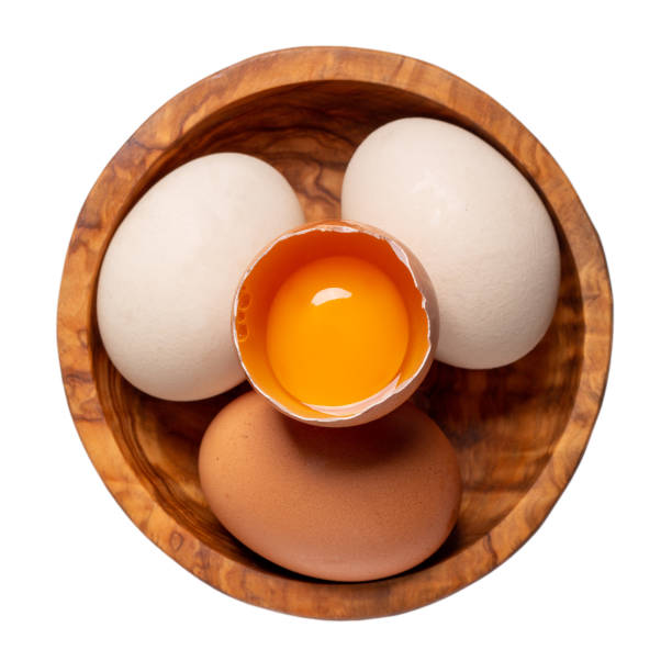 istock Three chicken eggs and half raw chicken egg with yolk  in wooden bowl isolated on white background. Top view. 1300999345