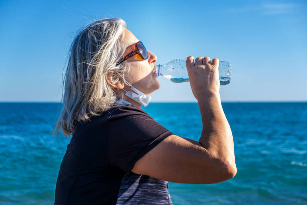 istock Old woman drinking water on the beach 1301000703