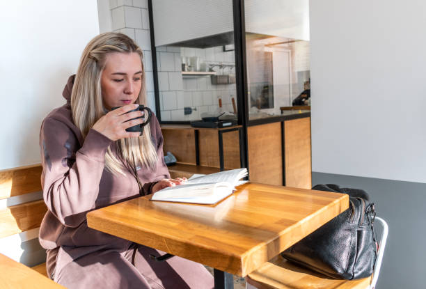 istock Young woman in a comfortable tracksuit is reading a paper book while drinking coffee in a cafe. 1301002187
