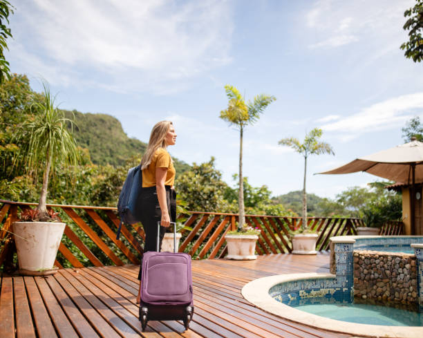 Young woman arriving at a tropical resort for her vacation Smiling young woman with a wheeled suitcase arriving at a tourist resort in the tropics vacation rental stock pictures, royalty-free photos & images