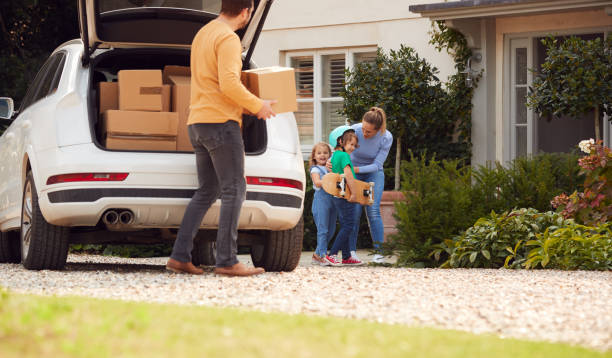 istock Family Outside New Home On Moving Day Unloading Boxes From Car As Son With Skateboard Helps 1301004323