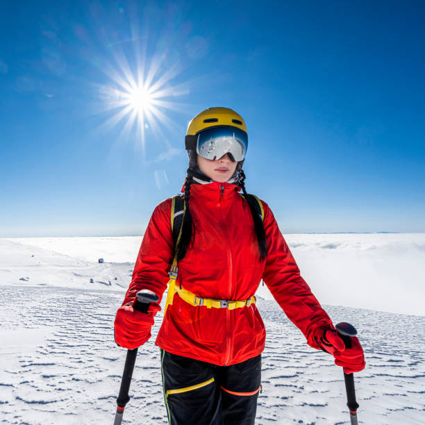 Beautiful female skier with yellow ski helmet, ski goggles, red jacket and black ski pants enjoys a fantastic winter day on the mountain covered with fresh snow.