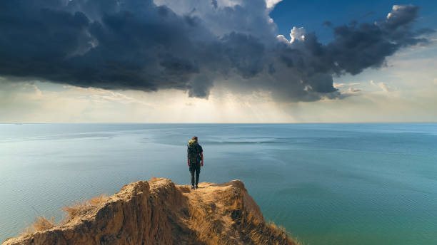 the hiker standing on a mountain against the rainy background - climbing men sea cliff imagens e fotografias de stock