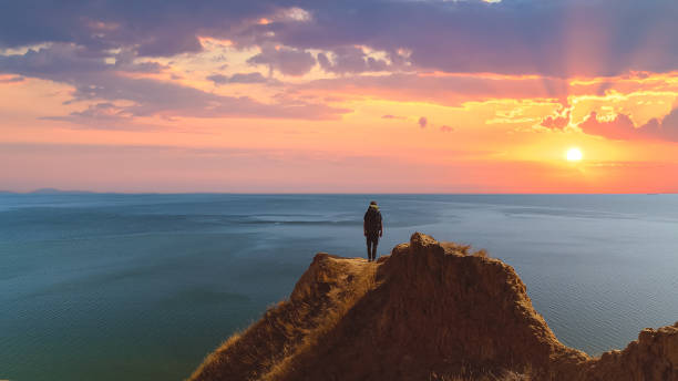 istock The man with a backpack standing on a mountain against a sea sunrise background 1301006319