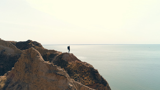 The hiker with a backpack standing on a mountain on the sea background