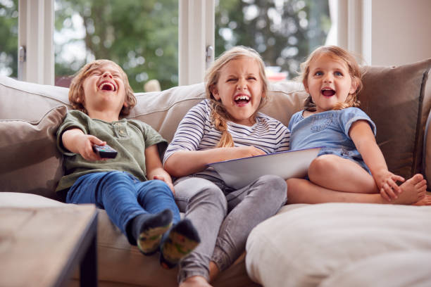 istock Three Children Sitting On Sofa At Home Laughing And Watching TV With Popcorn 1301006409