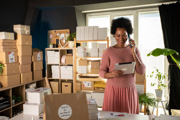 デジタルタブレットを使用して、携帯電話で話す笑顔の女性ビジネスオーナー - green business ストックフォトと画像