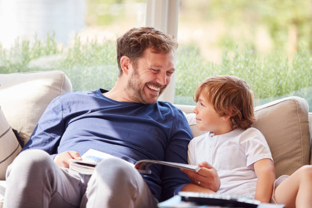 istock Father And Son Relaxing On Sofa At Home Reading Book Together 1301007691