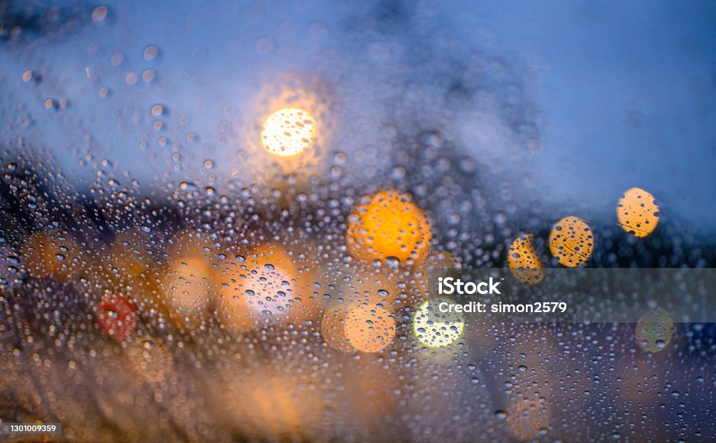 Rain droplets cling to the car glass at dusk Abstract, close up of raindrops on windshield with street light at night. Rain Stock Photo