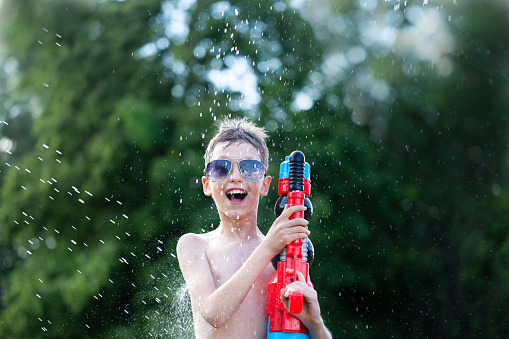 Smiling boy in glasses play with water gun at hot sunny summer day. Songkran thailand festival