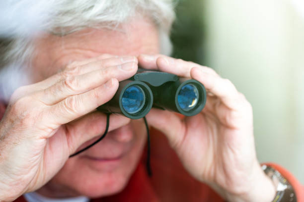 istock Senior man looking through binoculars at the window 1301012296